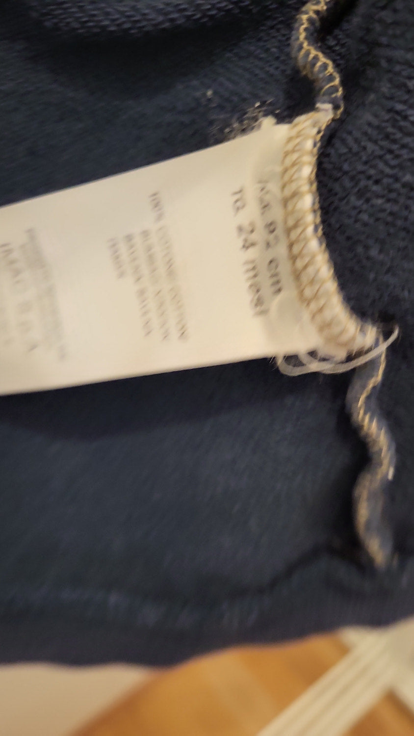 Close-up of a white size label reading 'Size 92 cm, 18 to 24 months', with the fabric composition and care text printed beneath it, too blurred to read in full.